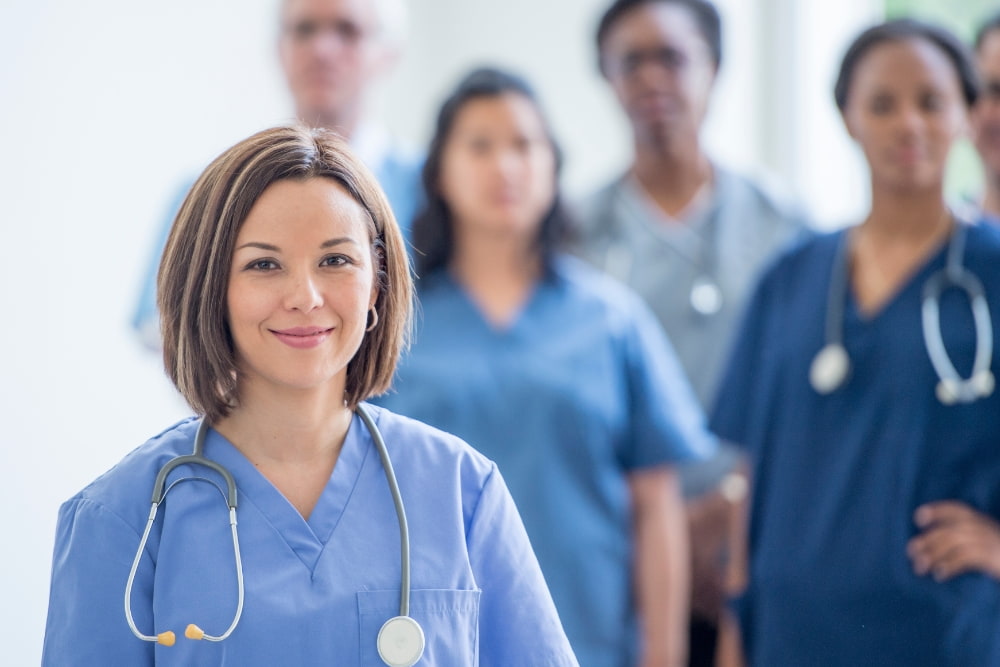 A group of healthcare professionals in scrubs, with a smiling woman in the foreground wearing a stethoscope.